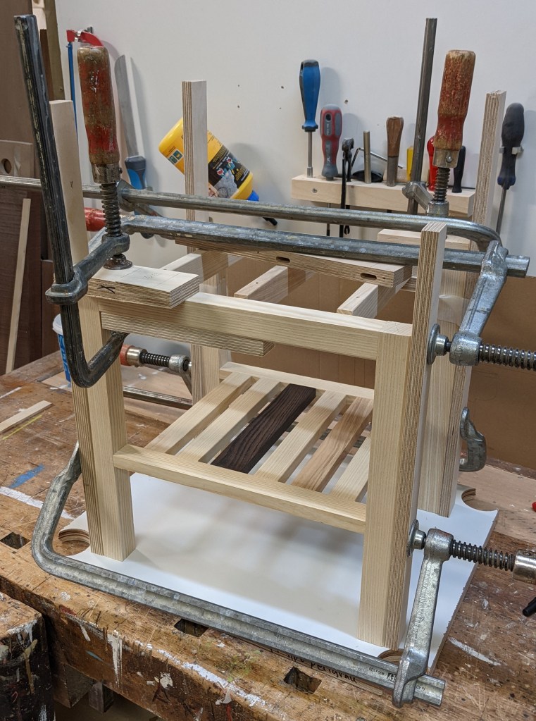 Gluing up the base of one of the cabinets with clamps. Wooden cauls are used to protect the wood for the metal clamps